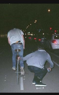 two men are riding their bikes down the street at night time while one man is on his bike