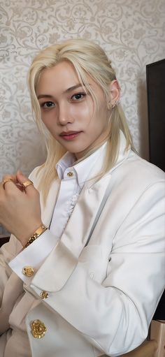 a woman with blonde hair wearing a white suit and gold bracelets sitting in a chair