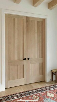 two wooden doors in a room with a rug on the floor and a table next to it