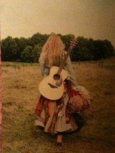 a woman with long blonde hair is holding an acoustic guitar in a grassy field while wearing a dress