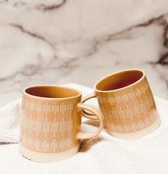 two coffee mugs sitting on top of a white towel next to a marble counter