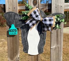 a black and white cow head with a bow on it's head hanging from a wooden fence