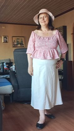 a woman in a pink top and white skirt standing on a hard wood floor next to a couch