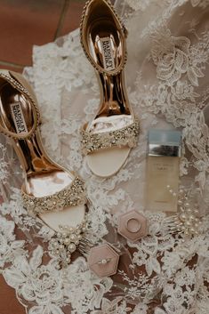 two pairs of shoes are sitting on a lace covered table cloth next to a bottle of perfume