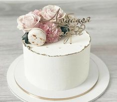 a white cake with pink flowers on top and the word love spelled in gold letters