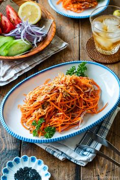 carrot salad with sesame seeds on a white and blue plate next to a glass of lemonade