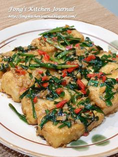 a white plate topped with chicken covered in green and red peppers on top of a wooden table