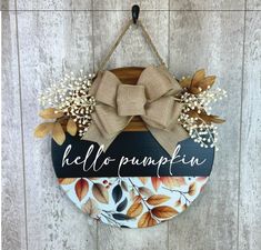 a sign hanging on the side of a wooden wall that says hello pumpkin with a bow