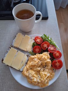 a white plate topped with eggs, toast and tomatoes next to a cup of tea