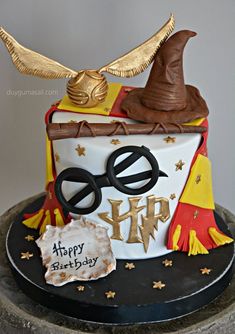 a harry potter birthday cake with glasses, wand and hat on top is decorated with gold stars