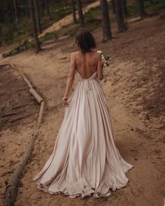 the back of a woman in a wedding dress walking down a dirt path near trees