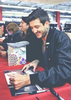 a man sitting at a table with an open book in front of him and smiling