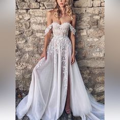 a woman standing in front of a stone wall wearing a white dress with an off the shoulder design