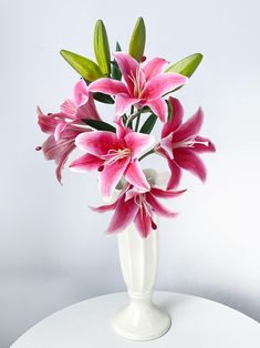 a white vase filled with pink flowers on top of a table