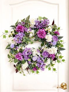 a wreath with purple and white flowers hanging on a door