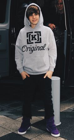 a young boy wearing a grey hoodie and black sweatpants standing in front of a van