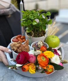 an arrangement of flowers and fruits in a bowl