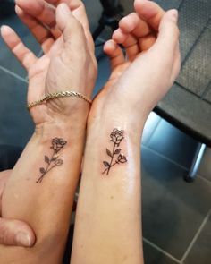 two people holding hands with tattoos on their wrists and one has a flower tattooed on it