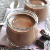 two jars filled with chocolate pudding sitting on top of a pink napkin next to silver spoons