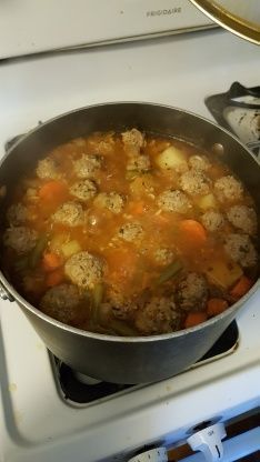 a pot filled with meatballs and carrots on top of a stove next to an oven