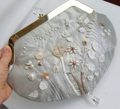 a hand holding a silver purse with flowers on it