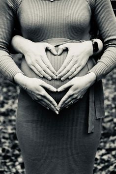 a pregnant woman is holding her stomach in the shape of a heart with both hands