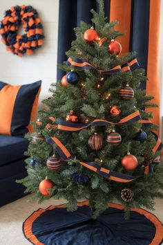 A navy blue Christmas tree with orange and navy ornaments paired with matching ribbons and a wreath in a cozy living space. Blue And Orange Christmas, Orange Christmas Decor, Room Decor Orange