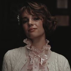 a woman with short hair wearing a white sweater and pink blouse is looking off to the side