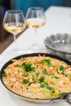 a pan filled with food sitting on top of a table next to two wine glasses