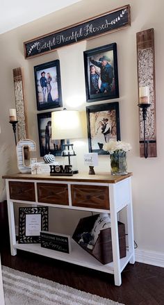 a white table topped with pictures and a lamp next to a wall filled with framed photos