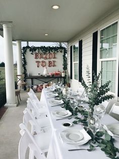 a long table set up with white plates and silverware for an outdoor bridal party