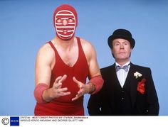 two men dressed in red and black are standing next to each other, one wearing a mask