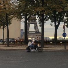 a man riding a motorcycle down the street in front of the eiffel tower