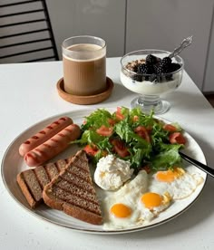 a white plate topped with eggs, toast and sausage next to a cup of coffee