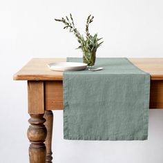 a wooden table topped with a plate and a vase filled with green plants on top of it