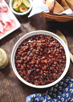 a white bowl filled with baked beans next to other food items on a wooden table