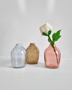 three different colored vases with a single white rose in one and a smaller pink one