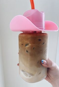 a person holding up a cup with a drink in it and a pink hat on top