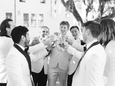 a group of men standing next to each other in front of a building holding wine glasses