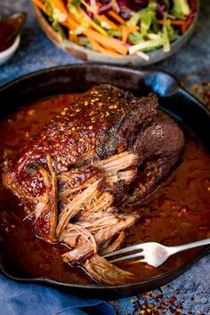 a large piece of meat is in a skillet with some sauce on it and a bowl of salad next to it