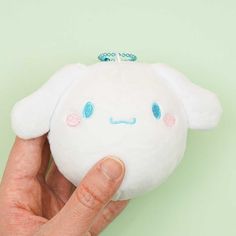 a hand holding a small white stuffed animal with blue eyes and pink ears, on a green background