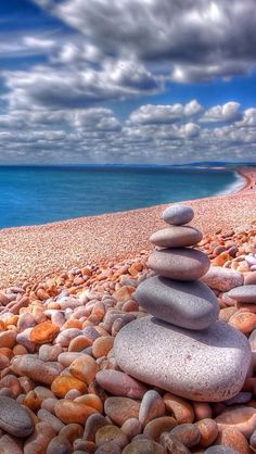 rocks stacked on top of each other in front of the ocean with clouds above them