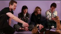 three people sitting on the floor petting two dogs and one is holding a cat