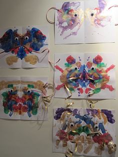 four cards with different colored handprints hanging from hooks on a white wall in front of them