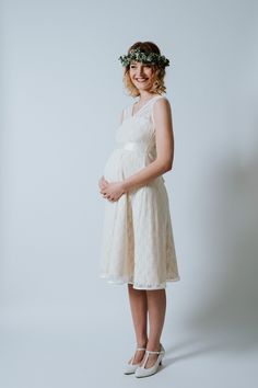 a pregnant woman wearing a white dress and flower crown