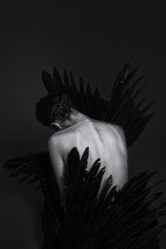 a black and white photo of a woman with feathers on her back in the dark