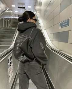 a woman is riding an escalator with her back to the camera and wearing a black hoodie