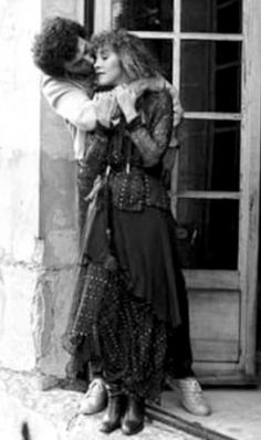 an old photo of two people embracing each other in front of a door and window