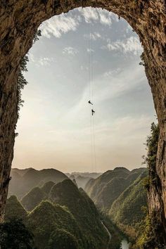 a man is suspended from the side of a cliff by a rope over a river