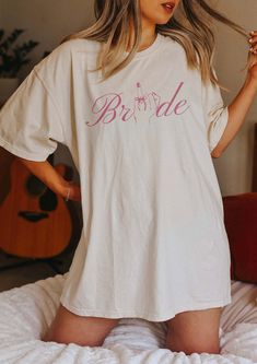 a woman standing on top of a bed wearing a white t - shirt with the word bride printed on it